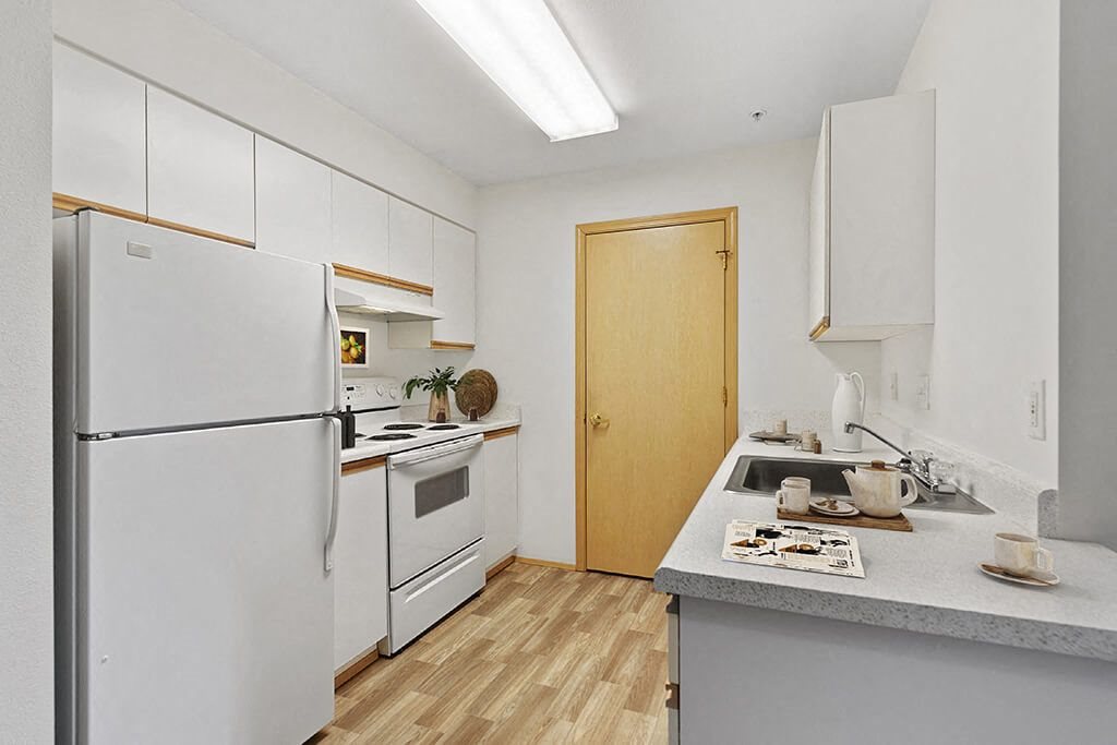 Kitchen with a white refrigerator freezer next to a stove top oven at Lakewood Meadows Apartments in Lakewood WA
